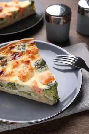 Piece of delicious homemade salmon quiche with broccoli and fork on wooden tableの写真素材