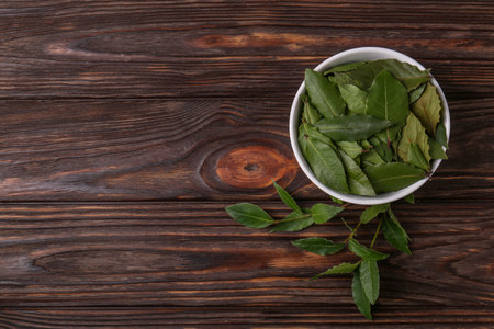 Fresh green bay leaves in bowl on wooden table, flat lay. Space for textの写真素材