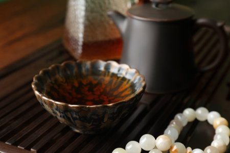 Cup with freshly brewed pu-erh tea and prayer beads on wooden tray, closeupの写真素材