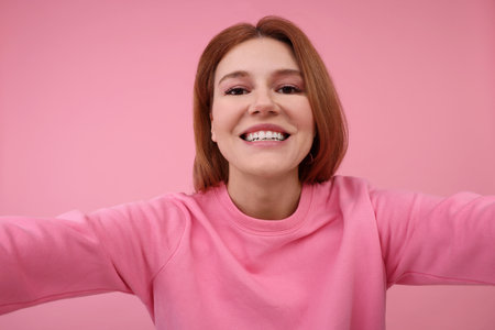 Beautiful woman taking selfie on pink backgroundの写真素材