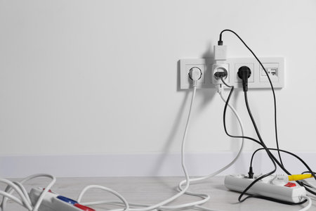 Different electrical plugs in sockets and power strip on floor indoors, space for text