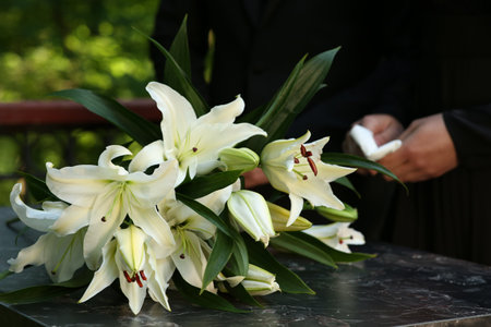 People near white lilies on granite tombstone at cemetery outdoors, closeup. Funeral ceremonyの写真素材