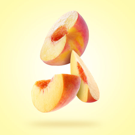 Cut juicy fresh peach falling on pale yellow backgroundの写真素材