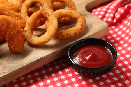Tasty ketchup with chicken nuggets and onion rings on checkered cloth, closeupの写真素材