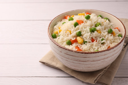 Bowl of delicious rice with vegetables on white wooden table, closeup. Space for textの写真素材