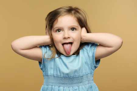Emotional little girl showing her tongue on beige background