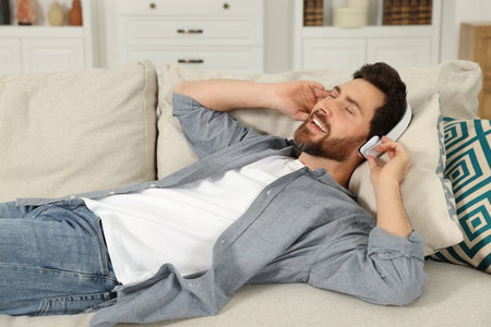 Happy man listening music with headphones on sofa indoorsの写真素材