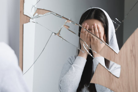 Woman covering face with hands near broken mirror. Mental problemsの写真素材