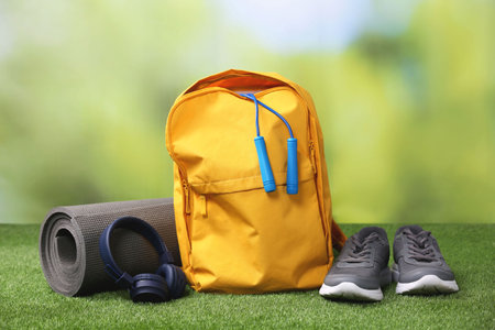 Backpack and different sports equipment on grass against blurred background