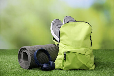 Backpack and different sports equipment on grass against blurred backgroundの写真素材