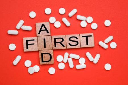Words First Aid made of wooden cubes and pills on coral background, flat layの写真素材