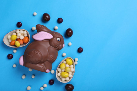 Chocolate Easter bunny, halves of eggs and candies on light blue background, flat lay. Space for textの写真素材