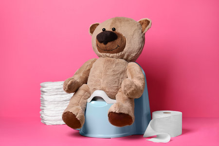 Teddy bear on baby potty, toilet paper and stack of diapers on pink backgroundの写真素材