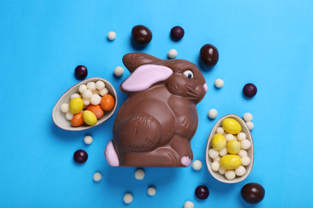 Chocolate Easter bunny, halves of eggs and candies on light blue background, flat lay
