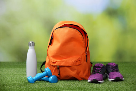 Backpack and different sports equipment on grass against blurred background