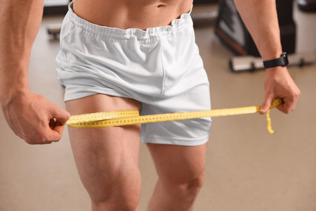 Athletic man measuring thigh with tape in gym, closeupの写真素材