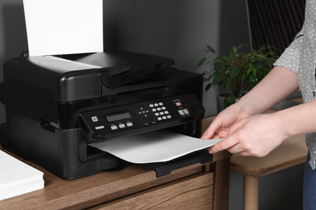 Woman using modern printer at wooden desk in home, closeup
