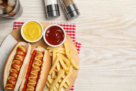 Delicious hot dogs with mustard, ketchup and potato fries on white wooden table, flat lay. Space for textの写真素材