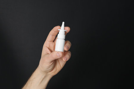 Man holding nasal spray on black background, closeup. Space for textの写真素材