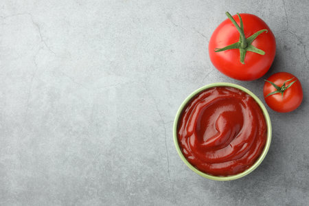 Bowl of tasty ketchup and tomatoes on light gray table, flat lay. Space for textの写真素材