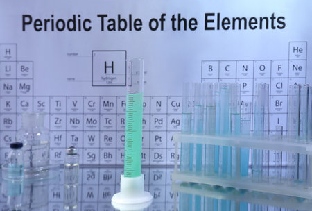 Graduated cylinder, bottles and test tubes in rack on mirror surface against periodic table of chemical elementsの写真素材