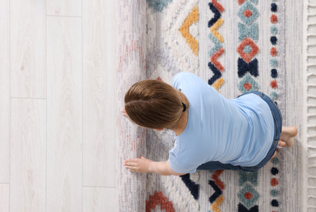 Woman unrolling carpet with beautiful pattern on floor in room, top view. Space for textの写真素材