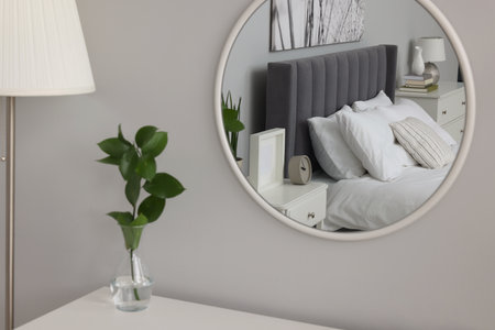 Reflection of large comfortable bed and bedside table in mirror on grey wallの写真素材