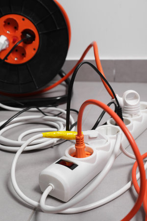 Extension cord reel plugged into power strip on gray floor indoors, closeup