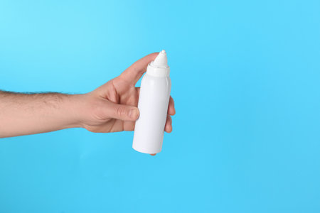 Man holding nasal spray on light blue background, closeup. Space for textの写真素材