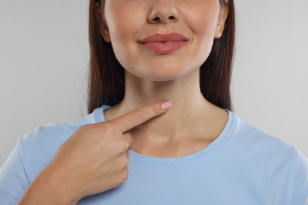 Endocrine system. Woman doing thyroid self examination on light gray background, closeup
