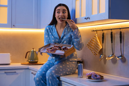 Young woman eating pizza in kitchen at night. Bad habitの写真素材