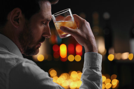 Man with glass of whiskey against blurred lights, closeupの写真素材