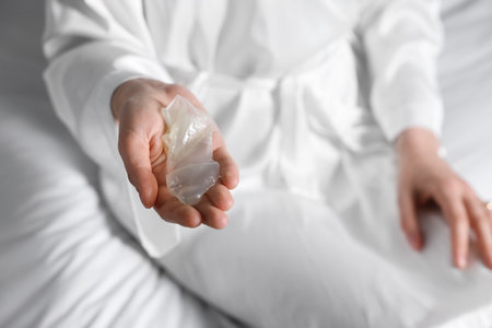 Woman holding unrolled condom on bed, closeup. Safe sexの写真素材