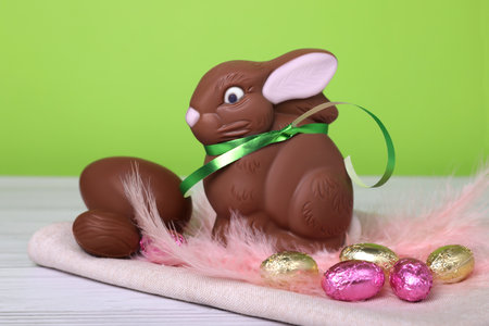 Chocolate Easter bunny, eggs and feathers on white wooden table against light green background, closeupの写真素材