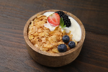 Delicious crispy cornflakes, yogurt and fresh berries in bowl on wooden table, closeup. Healthy...