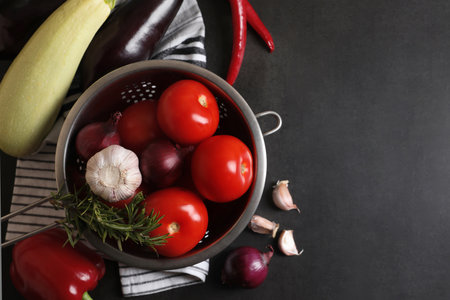 Cooking delicious ratatouille. Fresh ripe vegetables and colander on dark gray table, flat lay. Space for textの写真素材