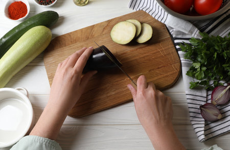 Cooking delicious ratatouille. Woman cutting fresh eggplant at white wooden table, top viewの写真素材