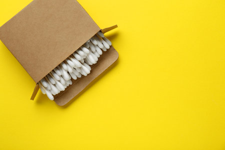 Cardboard box with cotton buds on yellow background, top view. Space for textの写真素材