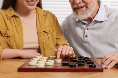 Playing checkers. Senior man learning woman at table in room, closeupの写真素材