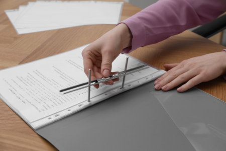 Woman fixing folder with punched pockets at wooden table, closeupの写真素材