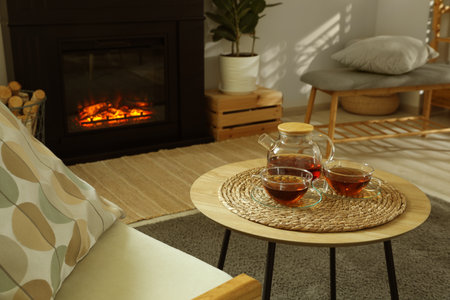 Teapot and cups of drink on coffee table near stylish fireplace in cozy living room. Interior designの写真素材