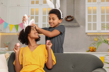 Happy African American mother with Easter eggs and her cute son in kitchenの写真素材