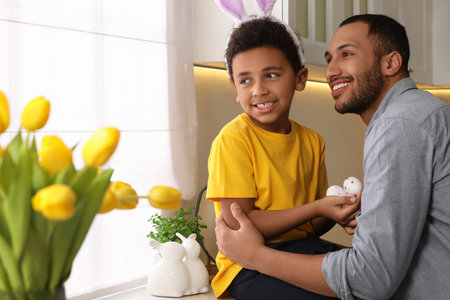 Happy African American father and his cute son with Easter eggs in kitchen