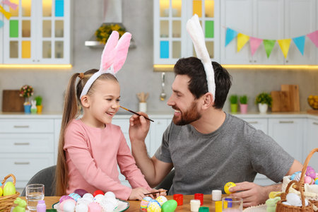 Father and his cute daughter having fun while painting Easter eggs at table in kitchenの写真素材