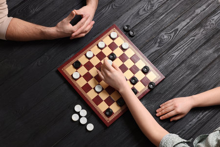 Man playing checkers with woman at black wooden table, top view