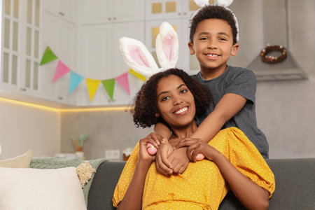 Happy African American mother with Easter eggs and her cute son in kitchenの写真素材