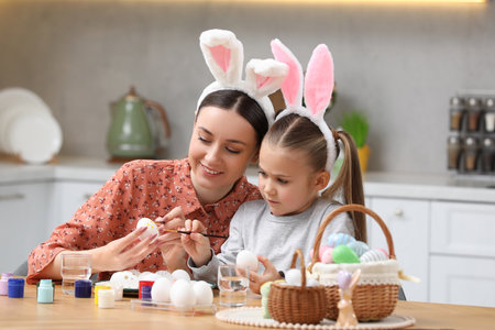 Mother and her cute daughter painting Easter eggs at table in kitchenの写真素材