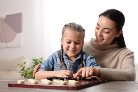 Playing checkers. Mother learning her daughter at table in room