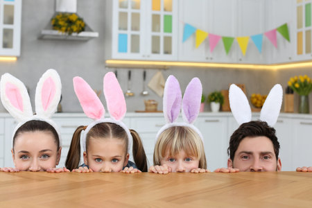 Happy family wearing bunny ears headbands and peeking over table in kitchen. Easter celebrationの写真素材