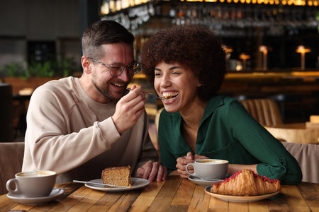 International dating. Handsome man feeding his girlfriend with cake in cafeの写真素材